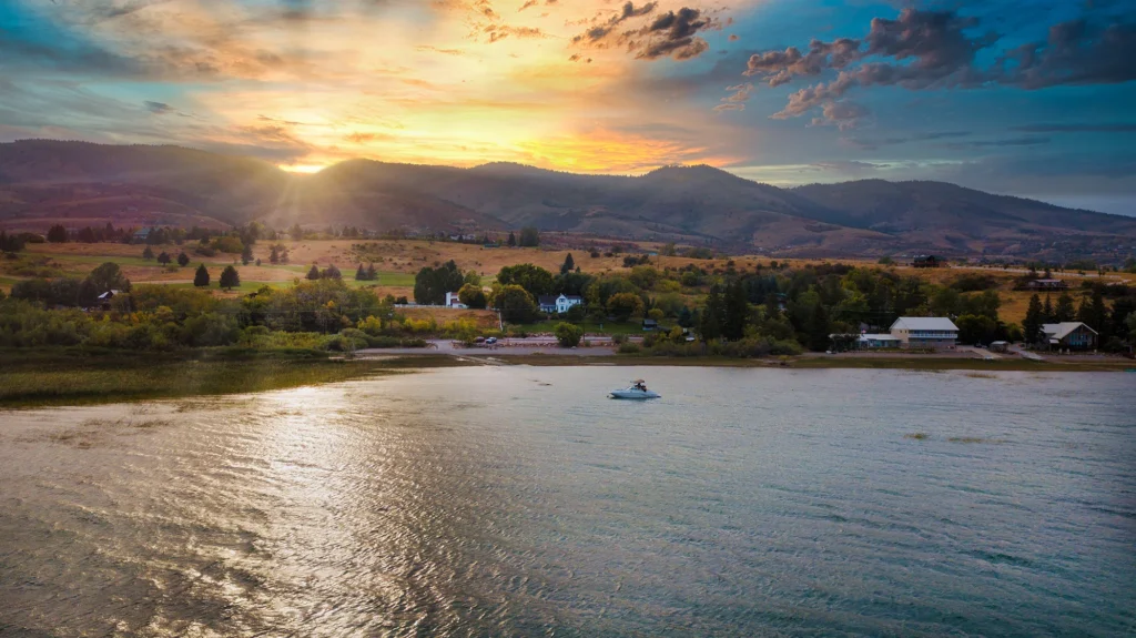 Sunset over Bear Lake with a boat on calm water, green trees, and rolling hills in the background