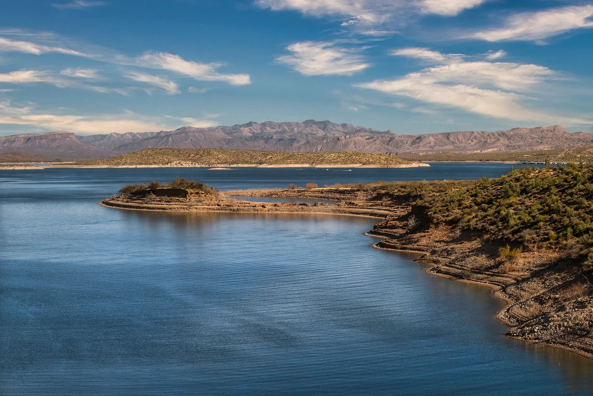 Roosevelt Lake shoreline with rocky desert banks, calm blue water, and mountains in the background