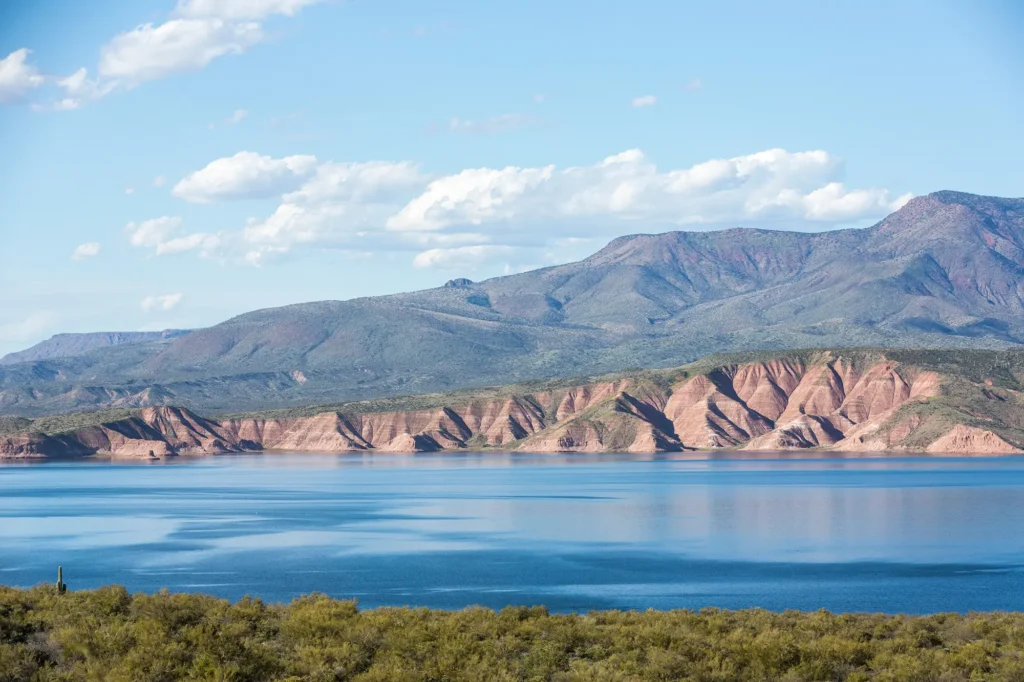 Roosevelt Lake with calm blue water, red and green layered cliffs, and desert mountains in the background