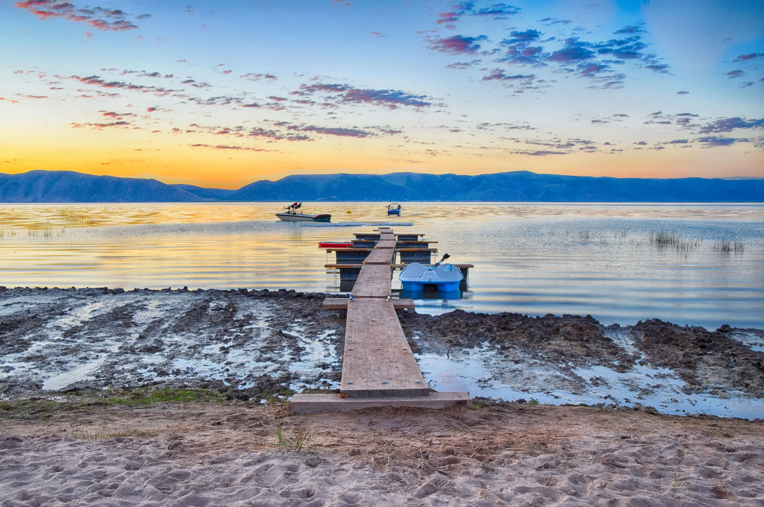 Wooden dock extending into Bear Lake at sunrise with two boats on calm water and mountains in the background